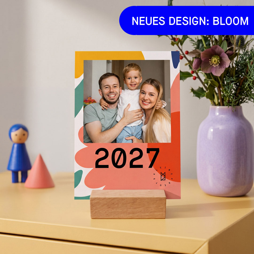 Tischkalender im Design Bloom mit bunten Blütenformen auf einer Kommode, daneben eine lila Vase mit Trockenblumen und eine Holzfigur — Kleine Prints