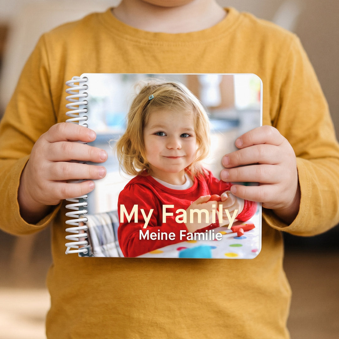 Kleine Kinderhände halten das quadratische Fotobuch für internationale Familien mit zweisprachigem Titel im Format 14 mal 14 Zentimeter